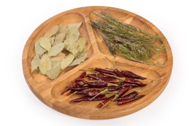 Kurumuş defne yaprakları, kırmızı biber ve biberiye kabukları beyaz arka planda üç bölümlü ahşap bölmeli tabakta.