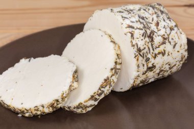 Çeşitli süt karışımlarından yapılmış yumuşak peynir parçaları ve farklı otlarla kaplanmış kahverengi bir tabakta, seçici bir odak noktasında.