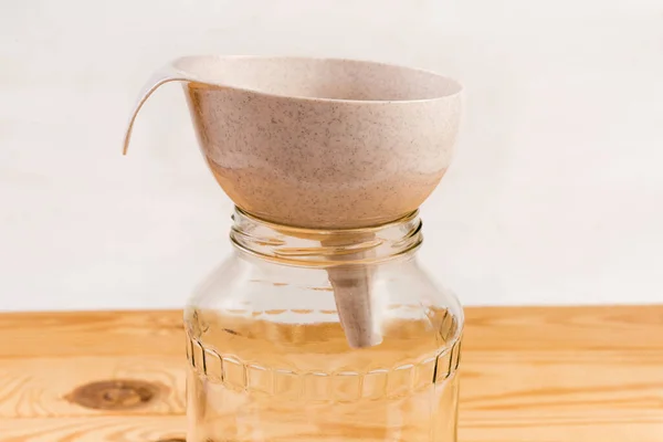 Plastic kitchen funnel for pouring liquids and powders on the mouth of empty glass jar on a rustic table, side view