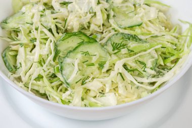 Dilimlenmiş taze lahana, salatalık, soğan ve doğranmış yeşil sebze salatası beyaz kasede, seçici odak noktasında yakın plan.