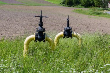 Açık havadaki iki valf, yeraltı doğal gaz boru hattının sarısına boyanmış metal borularda güneşli bir günde çimlerin arasında kapakçığı durdurur.