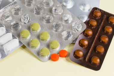 Diğer farklı hapların yanında, sarı bir yüzey üzerinde kısmen kullanılmış su toplayan iki kırmızı hap, seçici bir odak noktası.