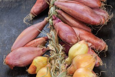Taze toplanmış kırmızı soğan demeti ve sırayla örülmüş soğan soğanları siyah yüzey üzerinde uzanıyor.