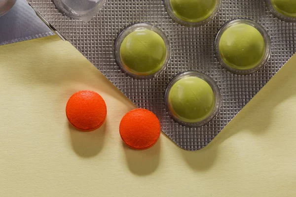 Green pills in partly used blister pack and two red pills separately on an yellow surface, top view close-up