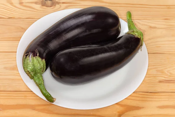 两个新鲜收获的成熟的全紫色茄子放在木桌上的盘子里 — 图库照片