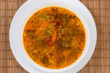 Baharatlı sebze çorbası servis ediliyor. Beyaz kâsede, bambu hasırının üstünde. Üst manzara.