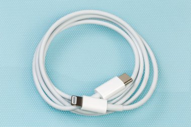 Mavi bir yüzey kenarlarında USB Tip-C ve Lightning ile sarmalanmış beyaz kablo