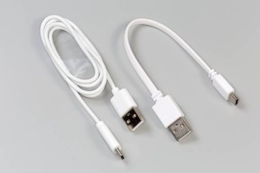 Kablolarda standart A ve standart C 'ye sahip iki farklı beyaz USB kablosu gri arka planda bitiyor.
