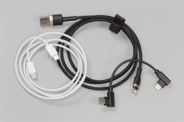Fişi USB Tip-C olan iki kablo ve bir ucunda Tip-A olan bir kablo ve gri arkaplandaki diğer kenarlarda Yıldırım tıkaçları.