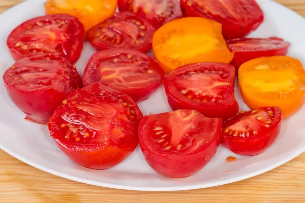 Halves of ripe red and yellow tomatoes on the white dish on the rustic table, side view of fragment close-up in selective focus