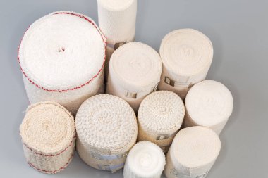 Modern dokuma elastik bandajlar seti farklı boyutlarda rulolara sarılmış, bazılarının alüminyum gerilebilir klipsleri gri bir yüzey üzerinde duruyor, üstten yakın çekim.