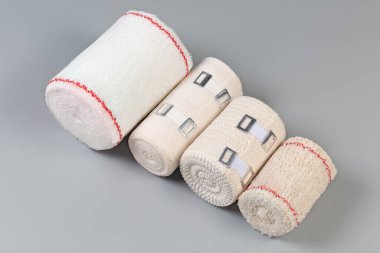 Çeşitli modern dokuma elastik bandajlar farklı boyutlarda ve kumaş yapılarda, bazılarının alüminyum gerilebilir klipsleri gri arka planda rulolara sarılı.