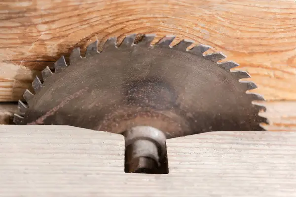 Circular steel saw blade for cutting wood mounted on an old table saw with wooden saw base, view close-up with shallow depth of field in selective focus