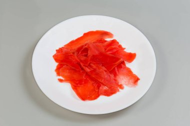 Kırmızı turşulu, ince dilimlenmiş zencefil gri arka plandaki beyaz tabakta.