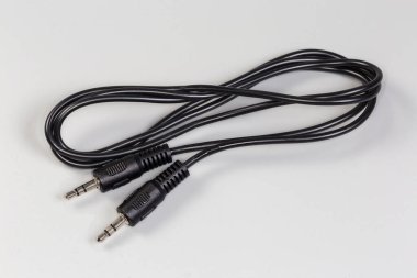 Stereo konnektörlü siyah analog ses kablosu kenarlarında mini kriko gri bir yüzey üzerinde uzanır.