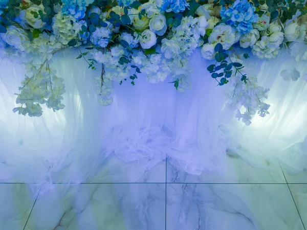 Part of the flower decoration with white and blue living flowers and other fresh and dried plant materials against the floor marble effect tiles with blue backlight