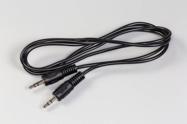 Rolled up black analog audio cable with stereo connectors mini jack on the edges lies on a gray surface close-up