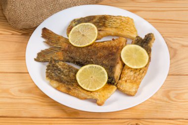 Kızarmış kuyruk parçası ve kırsal masada beyaz bir tabakta limon dilimleriyle süslenmiş diğer sazan dilimleri.