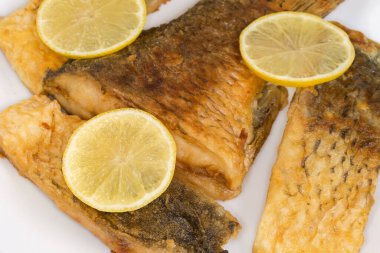 Beyaz bir tabakta limon dilimleriyle süslenmiş sazan balığı parçaları, seçici odak noktasında yakın plan.