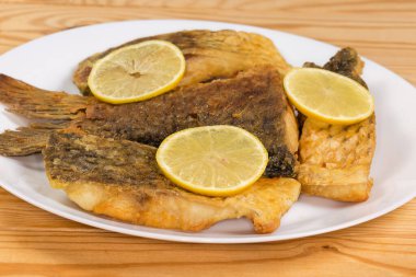 Kızarmış kuyruk kısmı ve limon dilimleriyle süslenmiş diğer sazan parçaları kırsal masada beyaz bir tabakta, yan görünüş ise seçici odak noktasında.