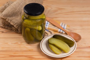 Bir tam ve bir yarım salatalık konservesi bir fincan üzerinde aynı salatalıklar kırsal masada kapalı cam kavanozda