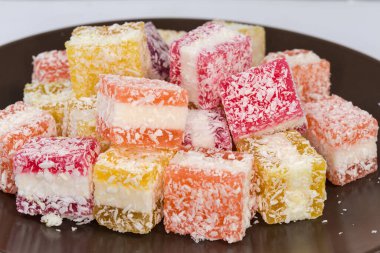 Şekerlemeler parça halinde çok renkli yumuşak şekerlemeler, marmelat olarak adlandırılan kahverengi tabağa hindistan cevizi serpiştirilmiş, yan görüş