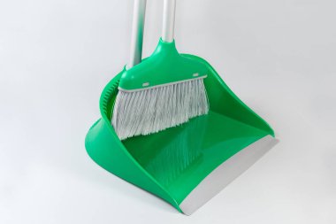 Gri tüylü yeşil plastik süpürge seti ve gri arka plandaki yerleri süpürmek için uzun metal saplı faraş.