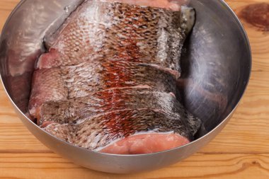 Taze soğumuş gökkuşağı alabalığının parçaları paslanmaz çelik mutfak kâsesinde kırsal bir masada, seçici odak noktasında parçalanmış.