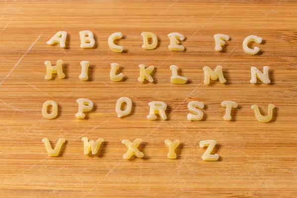 在竹子切菜板上按英文字母顺序排成大写字母的生面食 免版税图库图片