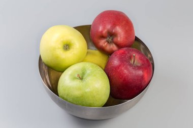 Tüm yeşil, sarı ve kırmızı elmalar gri arka plandaki paslanmaz çelik mutfak kasesinde.