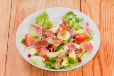 Jambon dilimlerinden yapılmış salata, haşlanmış bıldırcın yumurtası, taze yeşiller ve sebzeler kırsal bir masada beyaz bir tabakta.