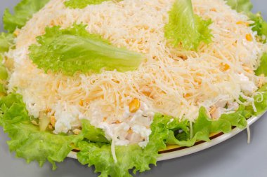 Haşlanmış tavuk etiyle yapılmış salata, ananas konservesi ve taze marulun üzerinde mısır rendelenmiş yumurta ve peynirle kaplanmış sarı tabakta, yakın plan.