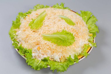 Haşlanmış tavuk etiyle yapılmış salata, ananas konservesi ve taze marullu mısır, rendelenmiş yumurta ve peynirle kaplanmış gri bir arka planda.