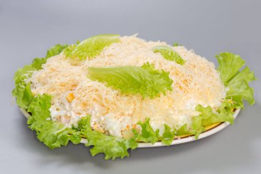 Kaynamış tavuk eti salatası, ananas konservesi ve taze marullu mısır, gri arka planda rendelenmiş yumurta ve peynirle kaplı, seçici bir odak noktasında yan görünüm.