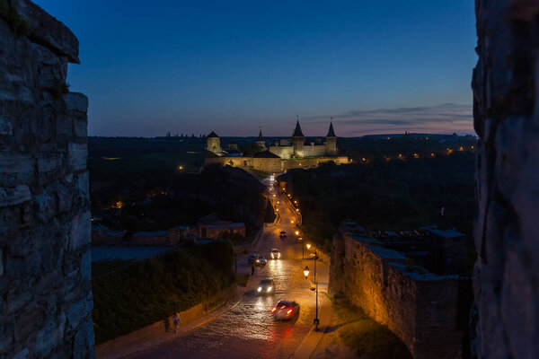 Ancient fortress of the 14-18th centuries with Castle Bridge on a foreground in Kamianets-Podilskyi city, Ukraine. General night view from the Old Town side in spring evening