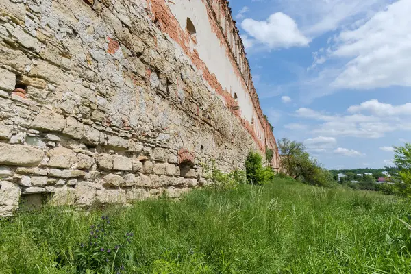 Ruins of the brick and stone defense wall of the mediaeval castle overgrown with different shrubs in Stare Selo village, Ukraine. View from the outside