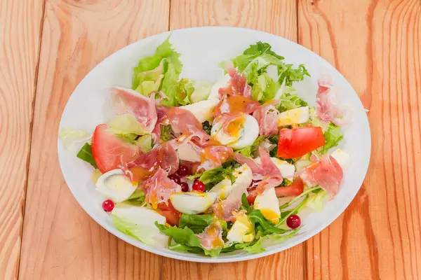 Jambon dilimlerinden yapılmış salata, haşlanmış bıldırcın yumurtası, taze yeşiller ve sebzeler kırsal bir masada beyaz bir tabakta.