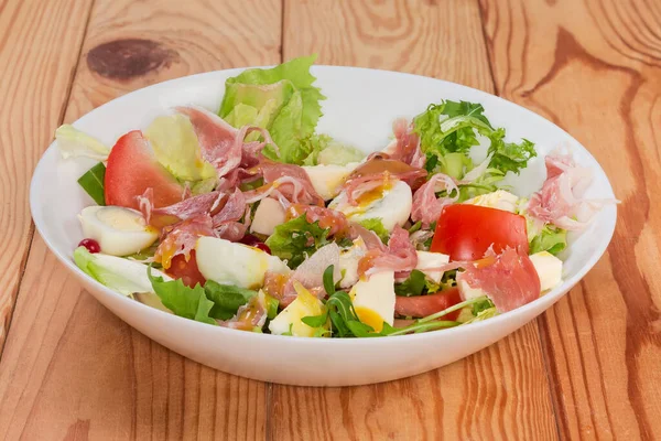 Jambon dilimlerinden yapılmış salata, haşlanmış bıldırcın yumurtası, taze yeşiller ve sebzeler kırsal bir masada beyaz bir tabakta, yan görünüşte.