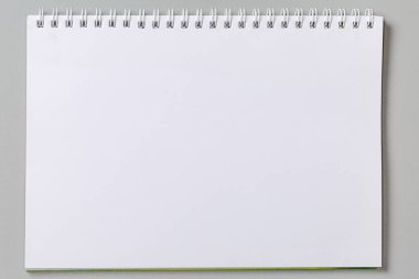 Okul egzersiz kitabının boş beyaz sayfası ya da gri arkaplanda tel sarmal bağlanmış kağıt defter, üst görünüm