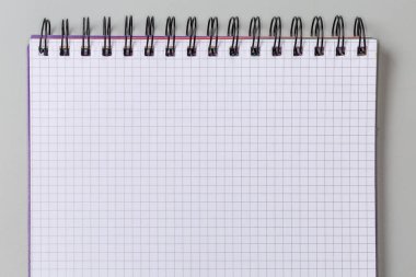 Okul egzersiz kitabının boş sayfası ya da kağıttan not defteri. Gri arkaplanda siyah kablo sarmalı, üst görünümde.