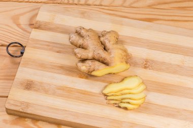 Tahta bir kırsal masada bambu kesme tahtasında kısmen doğranmış taze zencefil kökü.