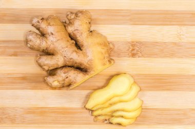 Bambu kesme tahtasının üzerinde kısmen dilimlenmiş taze zencefil kökü, yakın çekim.