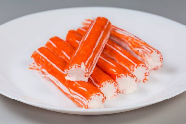 Norveç yengeç eti ve kıymalı okyanus balığını içeren yengeç çubukları gri arka planda beyaz bir tabakta, seçici odak noktasında yakın plan