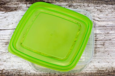Çatlamış eski bir tahta yüzey üzerinde kısmen çıkarılmış yeşil kapağı olan yeniden kullanılabilir şeffaf plastik gıda saklama kabı.