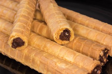 Çikolatalı kremayı siyah bir tabağa dolduran waffle tüpleri, seçici odak noktasında yakın plan.