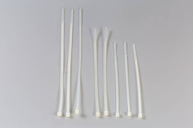 Several unfastened single-use nylon white translucent cable ties of different lengths on a gray background, top view clipart