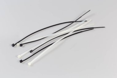 Several black and white unfastened single-use nylon white translucent cable ties on a gray background clipart