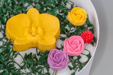 Çok renkli çikolata şekerlemeleri farklı çiçekler ve meyveler arasında yenmez yeşil plastik yapraklar arasında yuvarlak karton ambalajda, seçici odak noktasında parça yakın çekim