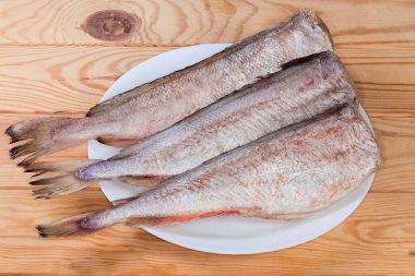 Kafası olmayan kırmızı morina leşleri, ahşap bir masada beyaz tabakta balık pullarından temizlenmiş.