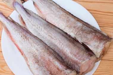 Kafası olmayan kırmızı morina leşleri, beyaz tabakta balık pullarından temizlenmiş ahşap bir kırsal masada, parçalı üst görünüm.